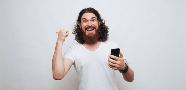 istock Cheerful man with beard holding phone and pointing away 1199751999