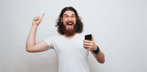 istock Excited berded man pointing up and holding phone 1199752837
