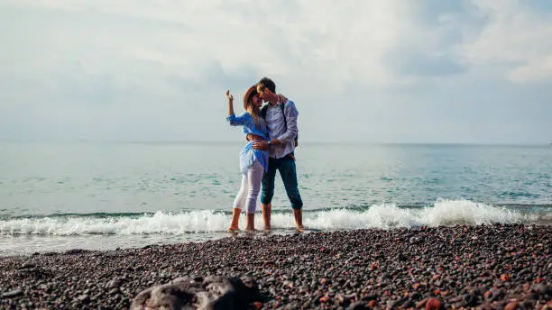 Photo of Valentines day. Couple in love kissing on honeymoon in Santorini island, Greece. People walking on beach by sea.