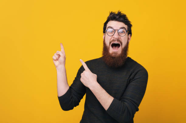 istock Amazed bearded man wearing glasses and pointing away at copyspace 1199754074