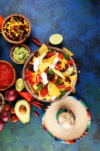 istock mexican nacho chips garnished with ground beef, guacamole, melted cheese, peppers and cilantro leaves in plate 1199765153