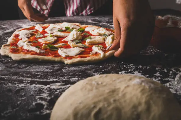 A closeup of a womans hands making an Italian pizza on a floured surface.