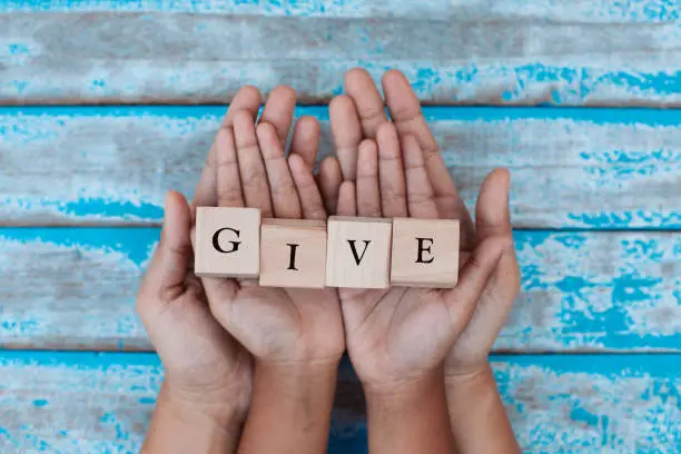 Photo of Alphabet letter wooden blocks with words GIVE in child and parents hands. Family and charity concept