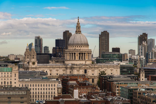 Grainy black and white analog photography of st paul's cathedral in london, showcasing the dome and a bell tower against a clear sky, with bare tree branches adding a touch of winter atmosphere