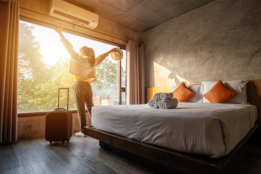 Retrato de mujer turística levantó las manos y de pie casi ventana, mirando a la hermosa vista con su equipaje en el dormitorio del hotel después del check-in. photo
