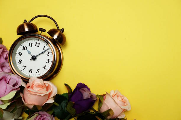 istock Alarm clock with Rose flower bouquet on yellow background 1199805016