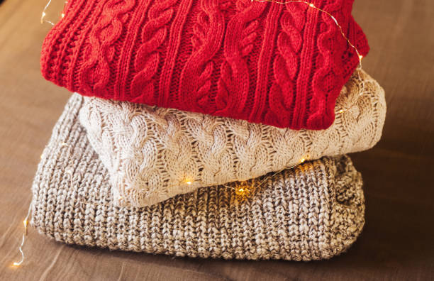 istock A pile of warm sweaters on the tissue background decorated with lights. 1199806549