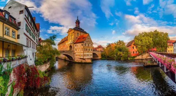 Amazing panoramic view of historic city center of Bamberg, Germany. Half-timbered Town Hall in the middle of rapid river, old buildings and bridge decorated by flowers. UNESCO World Heritage Site