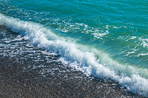 Sea wave with foam on a pebble beach. Wet bright shining different colored pebble stones and sea foam