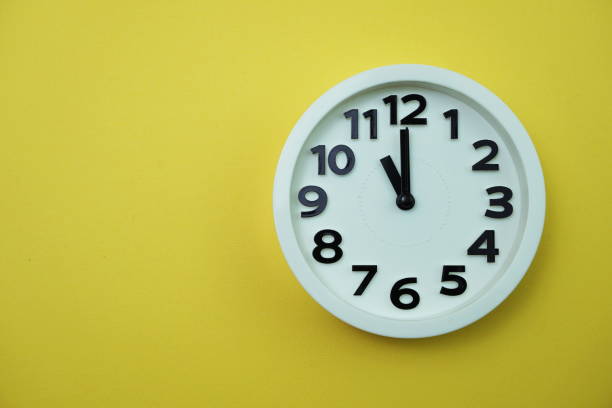 istock White round clock showing eleven o'clock on yellow background 1199820424