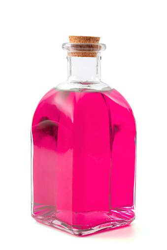 Magic spell and potion, apothecary elixir or deadly poison conceptual idea with vintage glass bottle containing pink or purple liquid isolated on white background with clipping path cutout