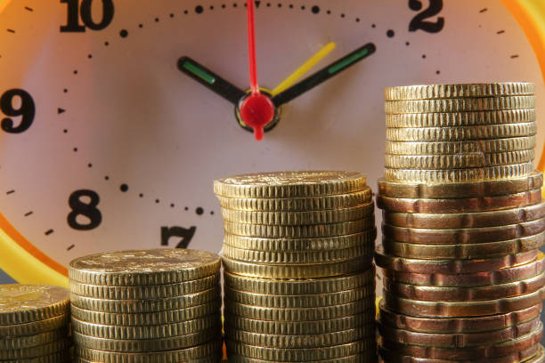 istock TAX TIME CONCEPT. Yellow clock and stack of coins over black background. 1199827981