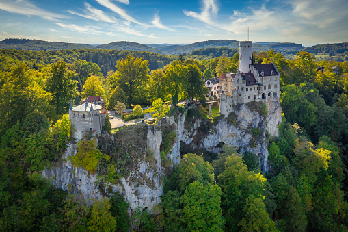 Honau - Reutlingen, Germany - September 30th, 2018: Aerial drone point of view over the Swabian Jura - Schwäbische Alb - with beautiful fairy-tale Castle Lichtenstein on top a steep rock a sunny late summer day. Unrecognizable tourists and visitors of from above. Swabian Alb, Reutlingen, Baden Wurttemberg, Germany
