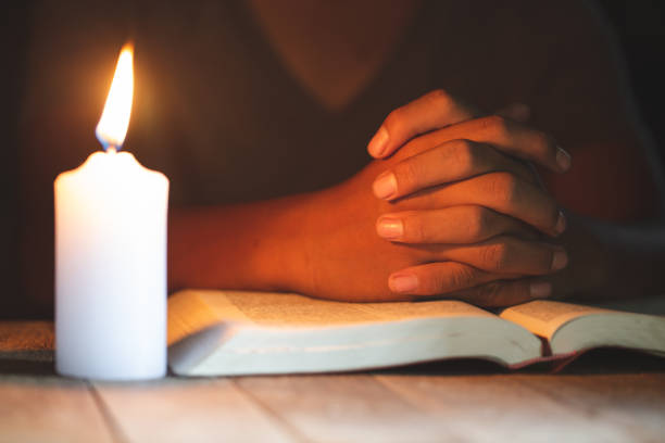 koncepcje religijne, młody człowiek modlił się na biblii w pokoju i zapalił świece do oświetlania. - praying bible church human hand zdjęcia i obrazy z banku zdjęć