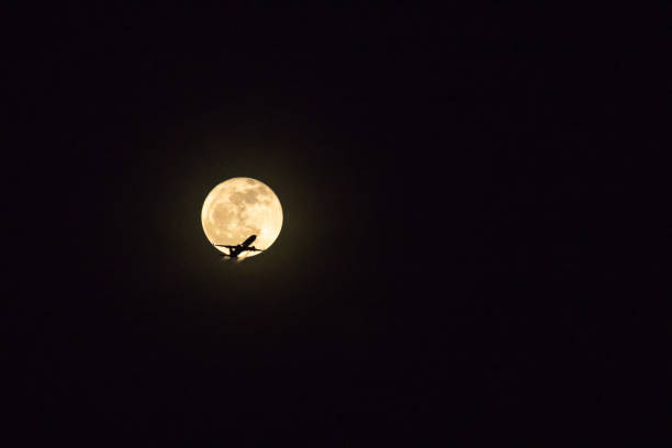 istock Silhouette plane flying against full moon in night sky. 1199829210