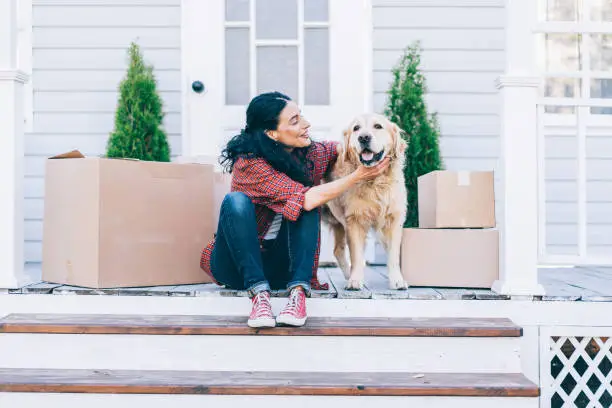 Мid adult woman moving to new house and sitting on the stairs and petting her golden retriever