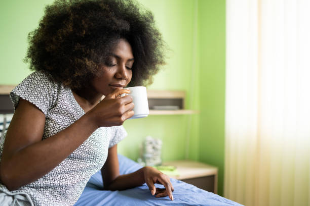 istock Afro woman sitting on a bed and drinking coffee 1199830975