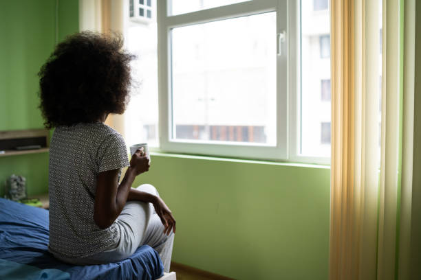istock Sad afro woman sitting on a bed and drinking coffee 1199830982