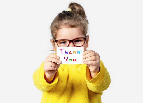 Adorable baby girl is holding a paper with a Thank you note. Silent communication concept