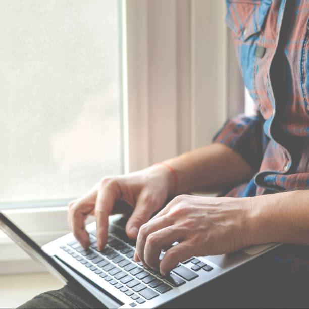 istock A man sits on a window sill with a laptop in his hands and works 1199843634