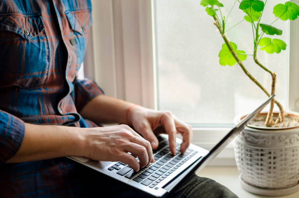 istock A man sits on a window sill with a laptop in his hands and works 1199843644