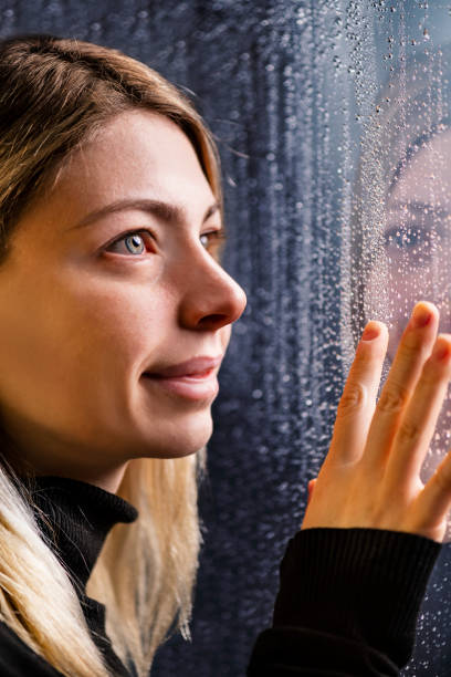 istock Thoughtful Young Woman Looking Through Window With Raindrops 1199850556