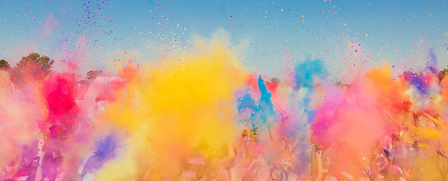 Diverse Crowd throwing bright colored powder paint in the air at Holi Festival Dahan event
