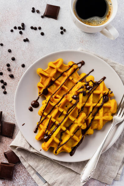 Pumpkin waffles with chocolate and icing sugar on light background and old rustic breakfast table. Top view.
