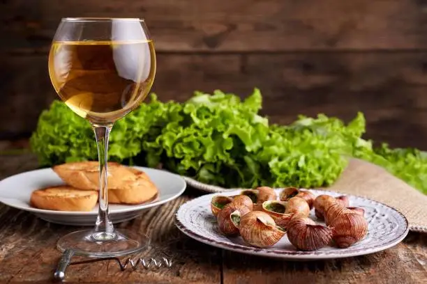 Escargots de Bourgogne - Snails with herbs butter on wooden background. Salad. Parsley. Glass of wine.