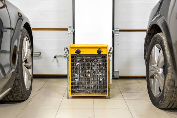 Big heavy industrial electric fan heater in double car garage interior. Two vehicles parked for winter storage in dry warm heating parking for cold winter season stock photo