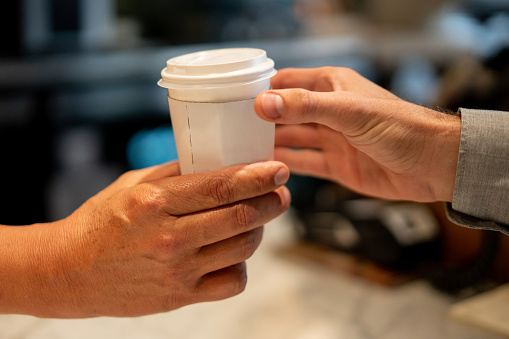 Close-up on a man selling coffee to a customer at a cafe - food service concepts