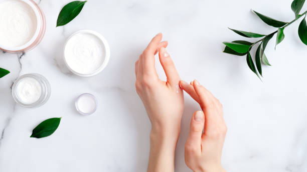 Cosmetic cream on female hands, jars with milk swirl cream and green leaves on white marble table. Flat lay, top view. Woman applying organic moisturizing hand cream. Hand skin care concept Cosmetic cream on female hands, jars with milk swirl cream and green leaves on white marble table. Flat lay, top view. Woman applying organic moisturizing hand cream. Hand skin care concept moisturizer stock pictures, royalty-free photos & images