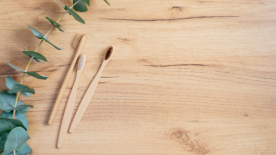 Biodegradable Eco-Friendly Natural Bamboo Charcoal Toothbrush and Green Eucalyptus Leaf on wooden table. Top view with copy space. Sustainable lifestyle. Zero waste, plastic free concept