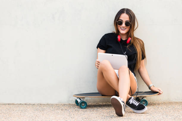 istock Young woman sitting on skateboard and holding tablet 1199863191