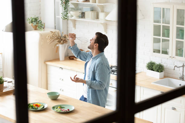 istock Overjoyed man having fun at kitchen, imitating microphone with whisk. 1199863495