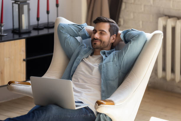 istock Peaceful young man daydreaming in comfortable armchair, holding computer. 1199863540