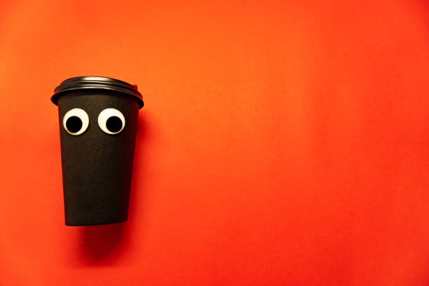 istock Black coffee paper cup with cap with googly plastic eyes are on red background, enough space for the text. 1199864520