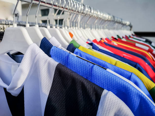 camisetas coloridas del equipo deportivo que cuelgan en los rieles de la ropa - traje deportivo fotografías e imágenes de stock