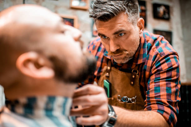 istock Young man getting his beard shaped by an electric trimmer in a barber shop 1199868281