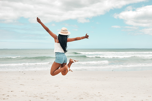 Rearview shot of a young woman jumping with her arms outstretched at the beach