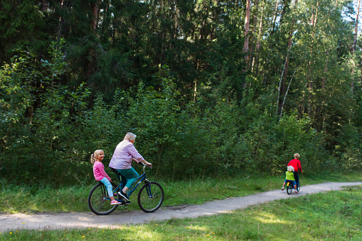 active senior grandmother with kids riding bikes in nature, active retirement
