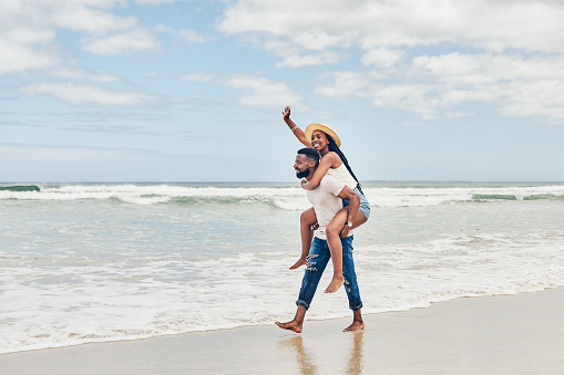Shot of a young man giving his girlfriend a piggyback ride at the beach