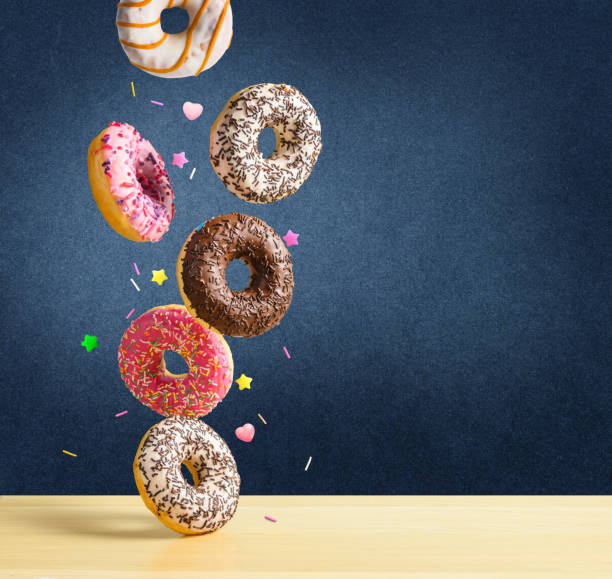 istock Flying donuts. Mix of multicolored sweet doughnuts with sprinkel falling on the table on dark blue textured background. 1199877379
