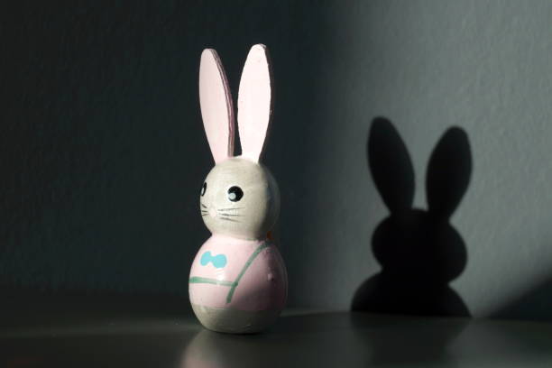 istock easter bunny is standing next to the wall. shadow on the wall. Conceptual image with shadow of cute easter rabbit on the wall. shadow concept on happy easter decoration background. 1199884036