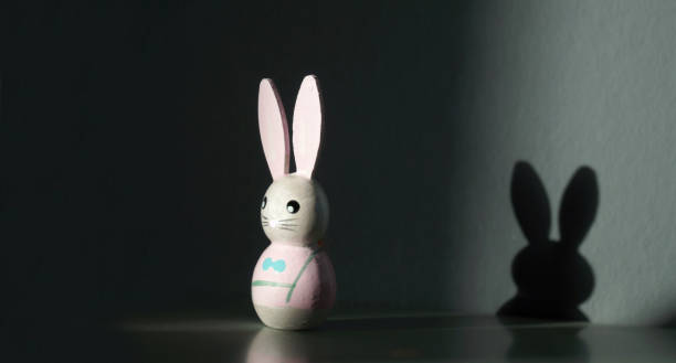 istock easter bunny is standing next to the wall. shadow on the wall. Conceptual image with shadow of cute easter rabbit on the wall. shadow concept on happy easter decoration background. 1199884080