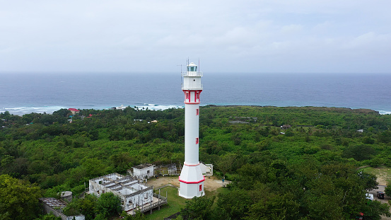 Lighthouse on a hill near the sea. Ocean coast with rainforest and lighthouse. Lighthouse on a tropical island, top view. Cape Bolinao Lighthouse, Luzon, Philippines. Summer and travel vacation concept.