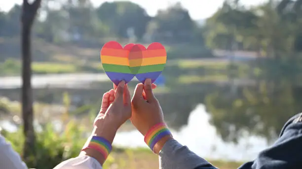 Photo of Closeup of LGBT couple while they are holding a rainbow hearts on hand. LGBT happiness concept.