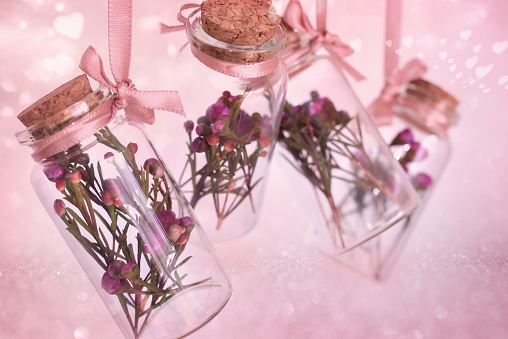 Small bottles with natural fragrant herbs. Hanging decoration on pink background with floating hearts for a mother's day gift. Selective focus