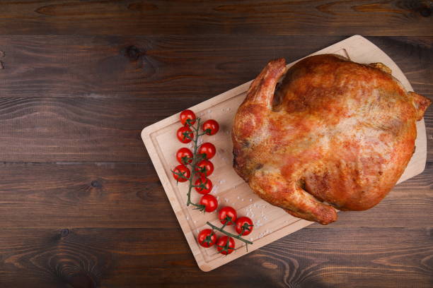 istock Baked whole chicken and cherry tomatoes on a wooden surface flat lay with copy space 1199887056