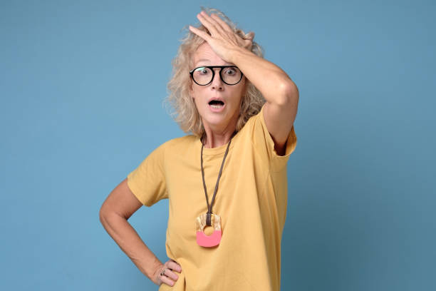 Excited mature blonde woman in glasses holding her head stock photo